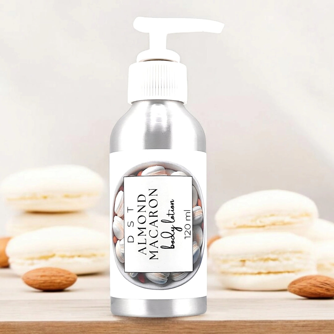 120ml bottle of Almond Macaron Body Lotion sitting on a white countertop with cream colored Almond macarons against a shadowy white background. 