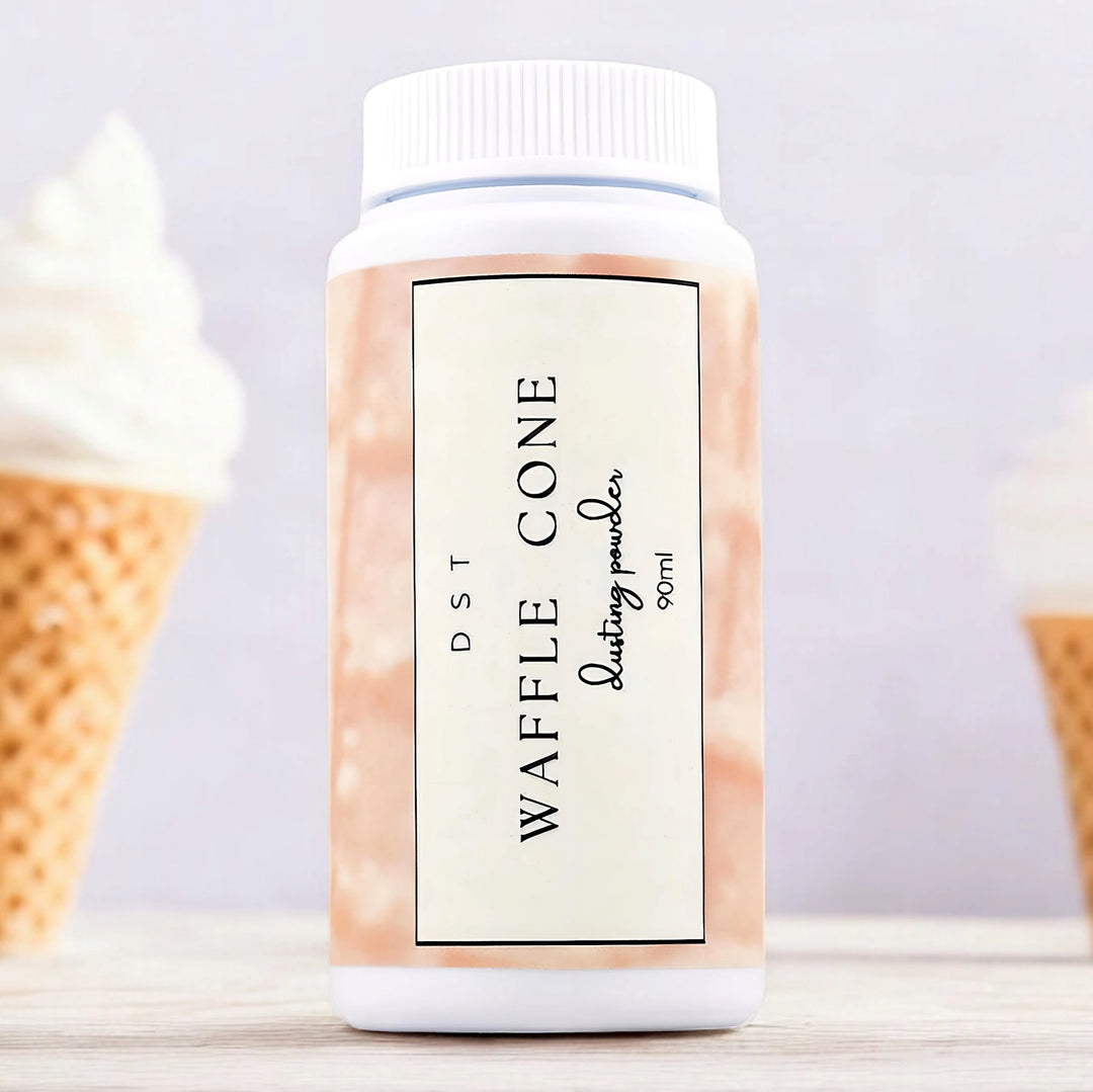 90ml bottle of Waffle Cone scented body powder sitting on a wood counter top with 2 vanilla ice cream cones against a light grey background. 