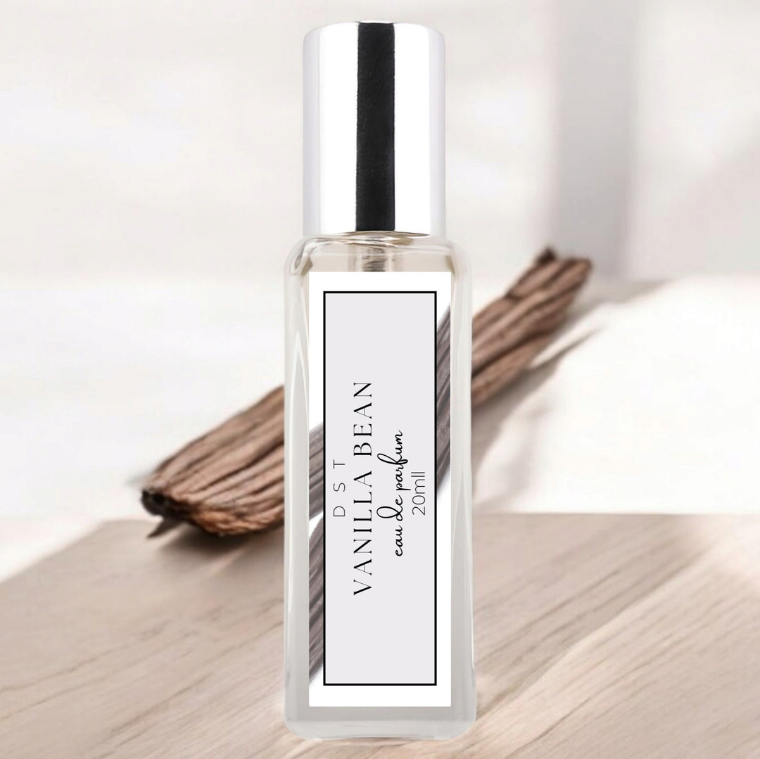 20ml bottle of Vanilla Bean parfum sitting on a wood counter top with vanilla beans against a  white background. 