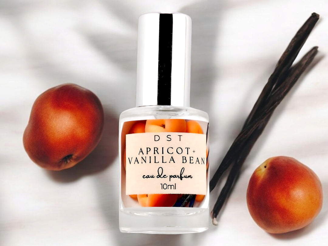 10ml bottle of Apricot and Vanilla Bean Eau de parfum sitting on a white background with 2 apricots and long vanilla beans.