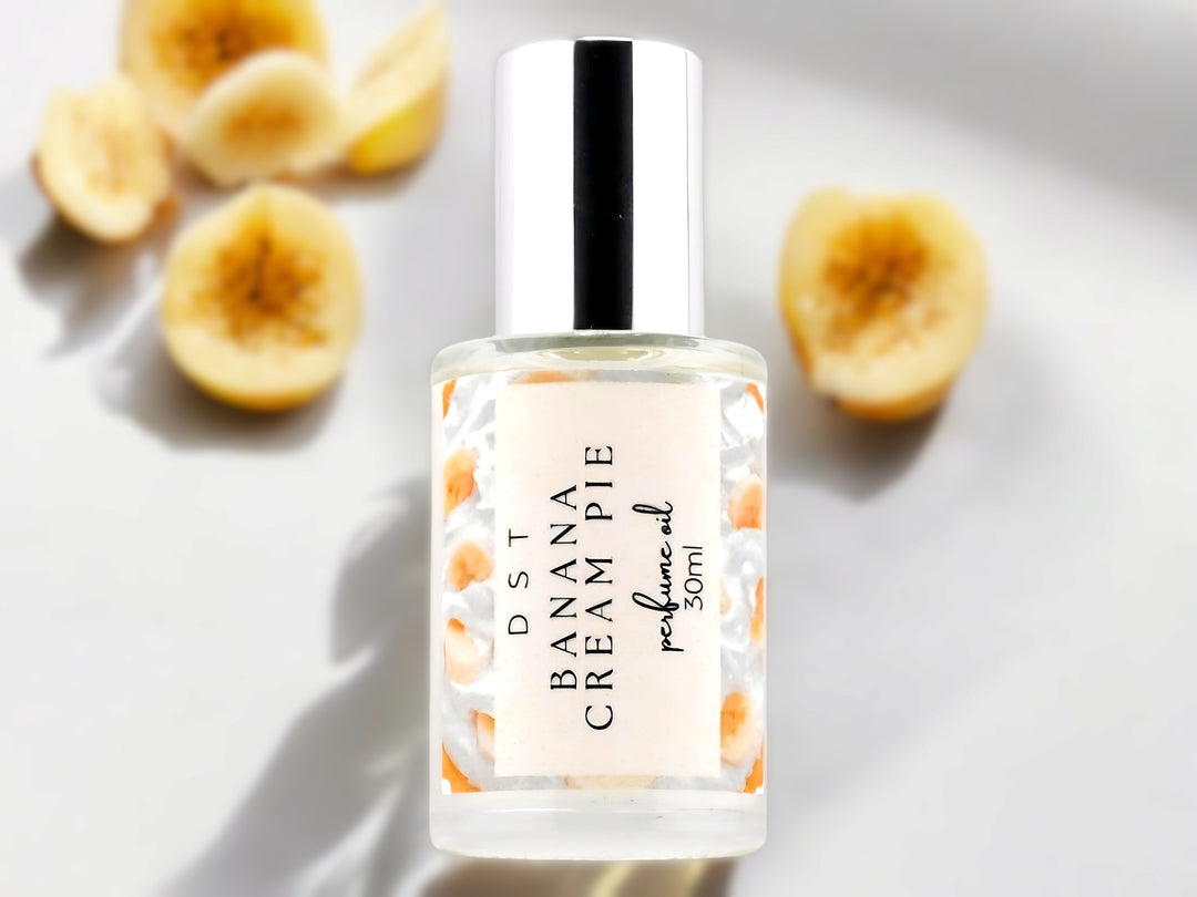 30ml bottle of Banana Cream Pie Perfume Oil sitting on a white surface with banana slices in the white shadowy background.