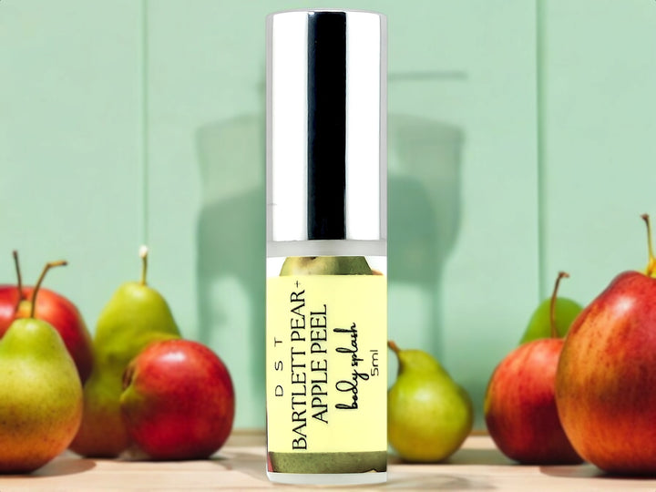 5ml bottle of Bartlett Pear and Apple Peel body splash spray sitting on wood countertop with red apples and green pears against a pastel green background.