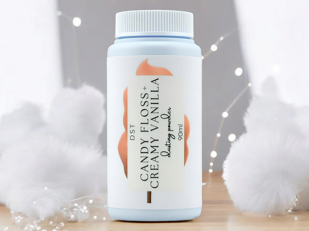 90ml bottle of Candy Floss and Creamy Vanilla body powder sitting on wood countertop with white cotton candy and twinkling fairy lights in the background.