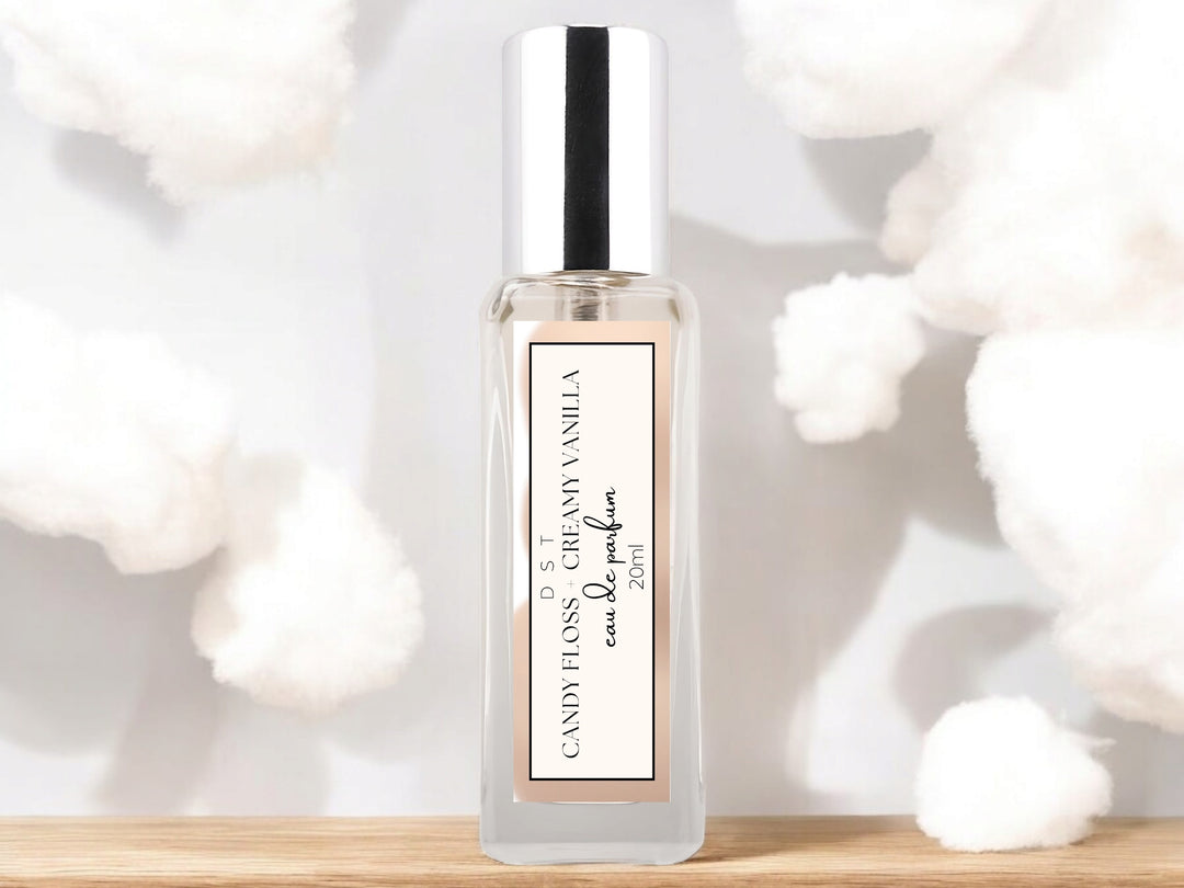 20ml bottle of Candy Floss and Creamy Vanilla Eau de parfum spray sitting on a wood countertop with white cotton candy against a white shadowy background.