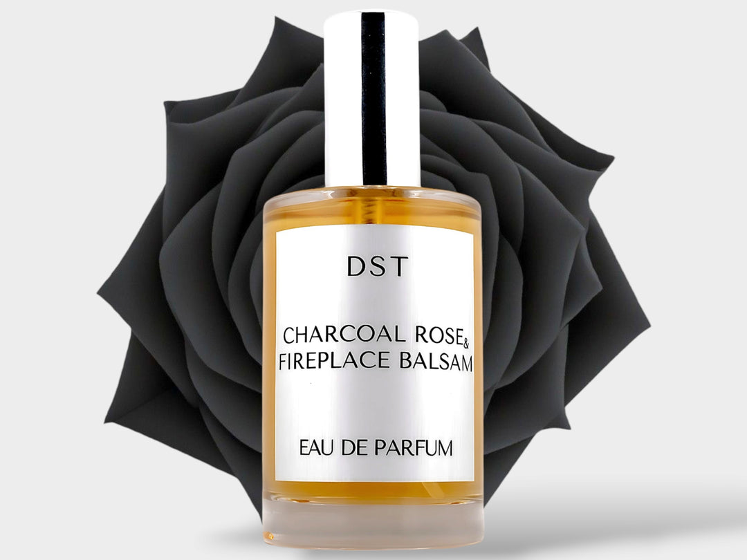 100ml bottle of Charcoal Rose and Fireplace Balsam Parfum sitting in front of a large black rose on against a light grey background. 