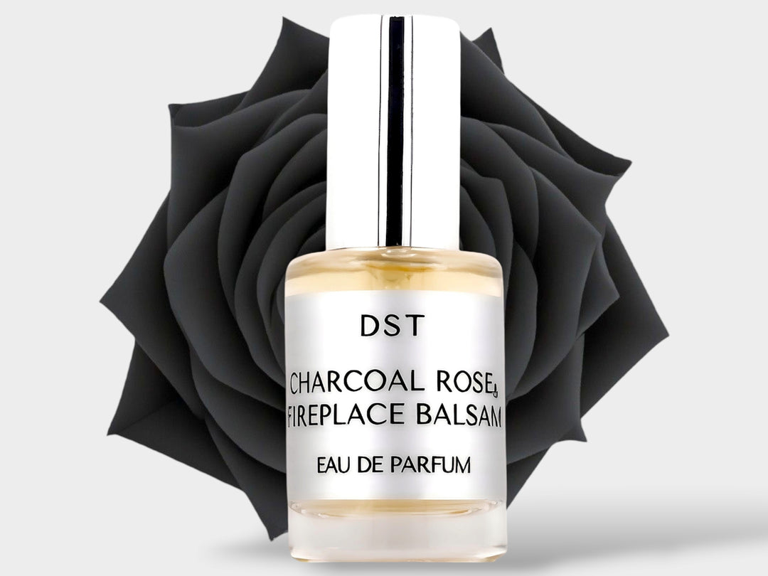 10ml bottle of Charcoal Rose and Fireplace Balsam Parfum sitting in front of a large black rose on against a light grey background. 