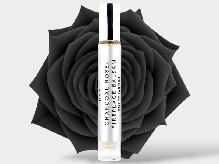 10ml bottle of Charcoal Rose and Fireplace Balsam Parfum sitting in front of a large black rose on against a light grey background. 