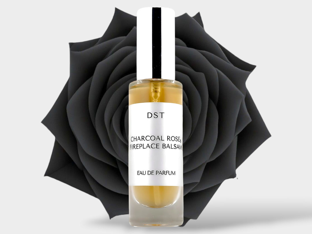 30ml bottle of Charcoal Rose and Fireplace Balsam Parfum sitting in front of a large black rose on against a light grey background. 