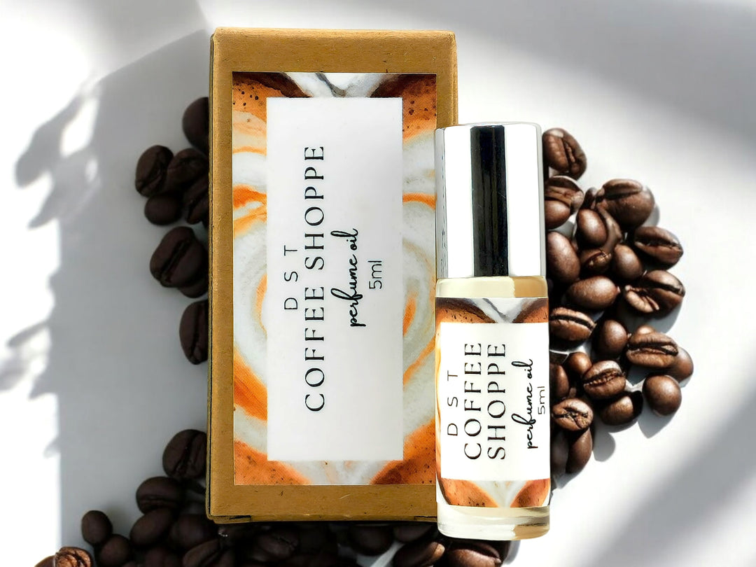 5ml bottle of Coffee Shoppe perfume oil and the box it is packaged in against white shadowy background with scattered coffee beans.