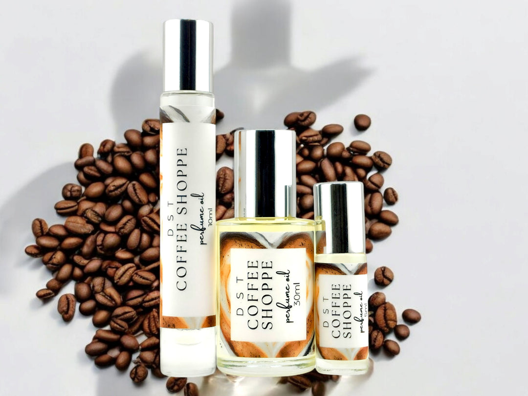 5, 10, and 30ml bottles of Coffee Shoppe perfume oil against white shadowy background with scattered coffee beans.