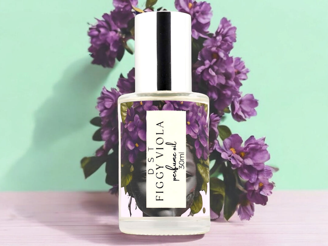 30ml Bottles of Figgy Viola perfume Oil sitting on a wood table with violets against a pastel green background.