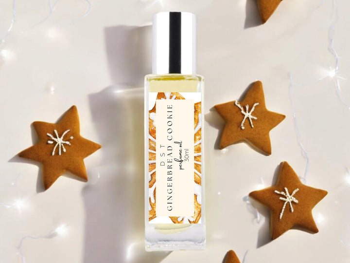 30ml bottle of Gingerbead Cookie perfume oil sitting on ivory backdrop with frosted star shaped gingerbread cookies and twinkling fairy lights in the background.