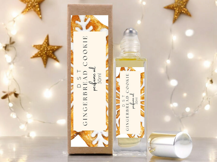 30ml bottle of Gingerbead Cookie perfume oil and the box it is packaged in sitting on wood countertop with gold glitter stars and twinkling white fairy lights against an ivory background.