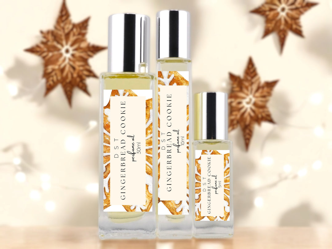 5, 10 and 30ml bottles of Gingerbead Cookie perfume oil sitting on wood countertop with decorated star shaped gingerbread cookies and twinkling white fairy lights against an ivory background.