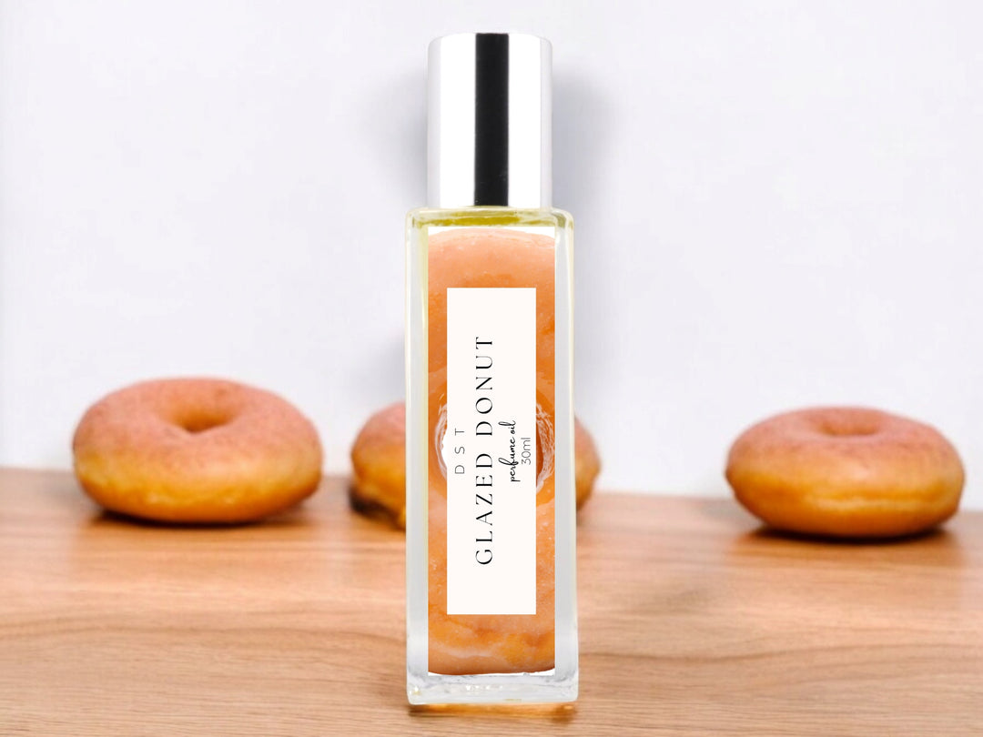 30ml bottle of Glazed Donut Perfume Oil sitting on a white surface with 3 glazed donuts against a shadowy white background.