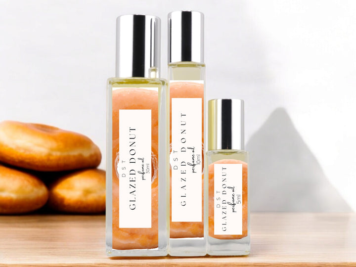 5, 10, and 30ml bottles of Glazed Donut Perfume Oil sitting on a white surface with 3 glazed donuts against a shadowy white background.