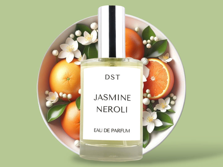 100 milliliter bottle of Jasmine Naroli perfume sitting in front of a large bowl filled with oranges and Jasmine flowers against a light green background.