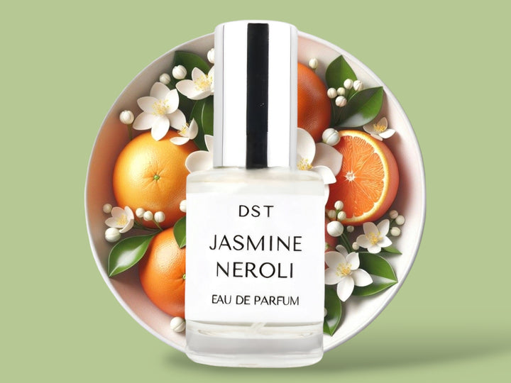 10 milliliter bottle of Jasmine Naroli perfume sitting in front of a large bowl filled with oranges and Jasmine flowers against a light green background.