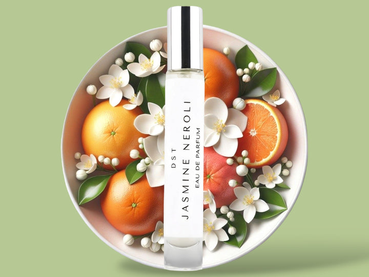 10 milliliter tall bottle of Jasmine Naroli perfume sitting in front of a large bowl filled with oranges and Jasmine flowers against a light green background.