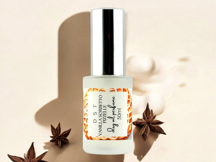 30ML bottle of Vanilla Sorbetto and Puzzelle Dry Oil Perfume Spray laying on a cream shadowy surface surrounded by star anise and whipped cream.