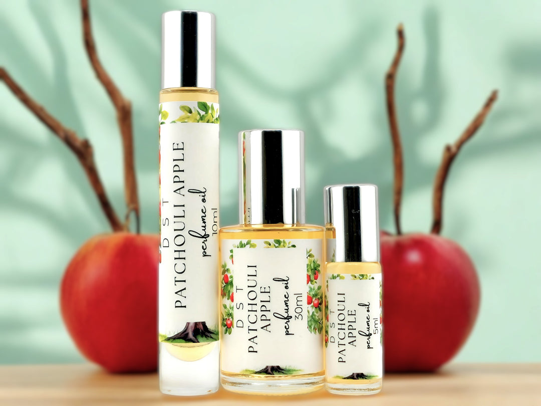 5, 10, and 30ml bottles of Patchouli Apple perfume oil sitting on wood countertop with red apples and cinnamon sticks in the light green background.