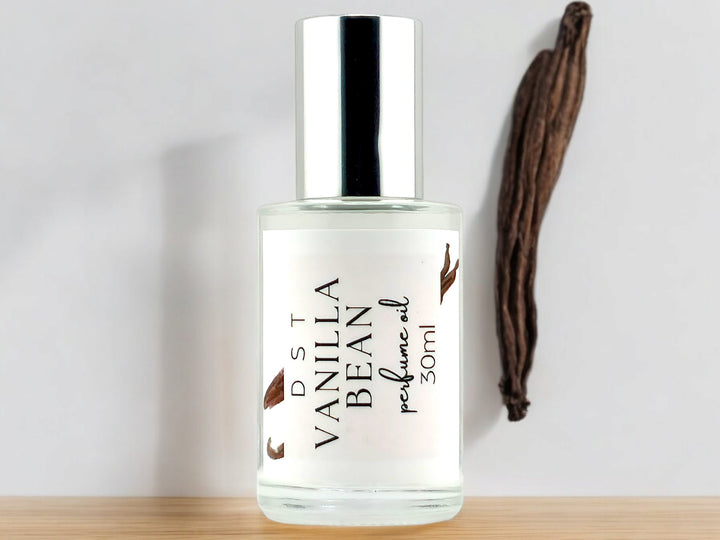 30ml bottle of Vanilla Bean perfume oil sitting on wood countertop with white background and vanilla bean prop.