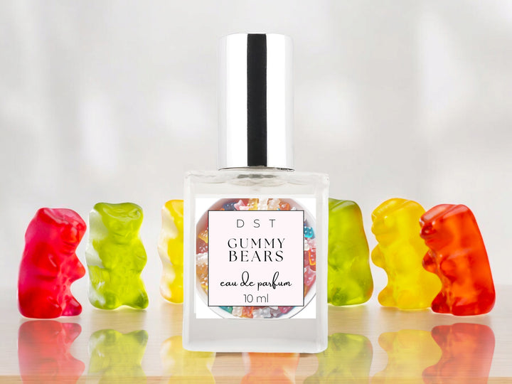 10ml bottle of Gummy bears parfum sitting on a wood counter top with bright colored Gummy bears behind it on a white shadowy background.