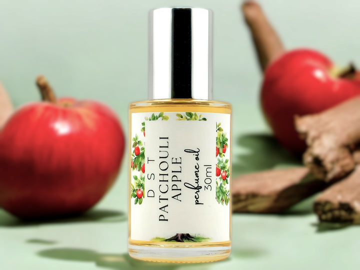 30ml bottle of Patchouli Apple perfume oil sitting on wood countertop with red apples and cinnamon sticks in the light green background.