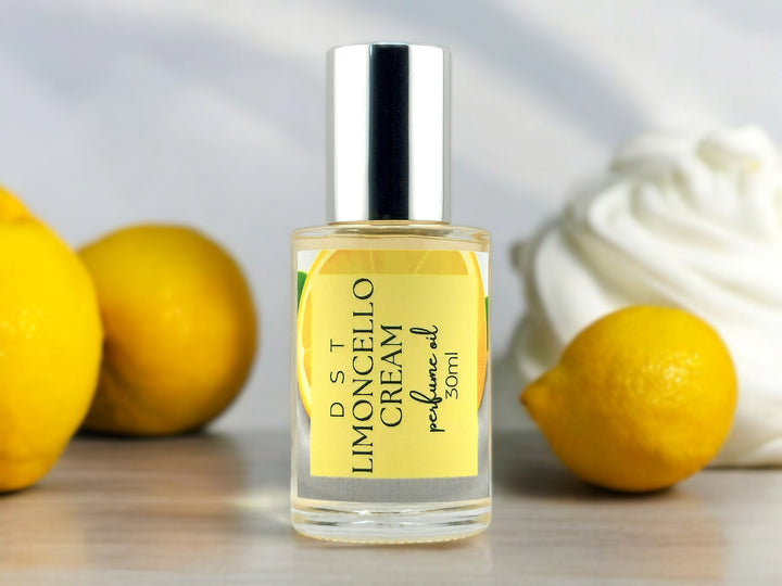 30ml bottle of Limoncello Cream perfume oil sitting on wood countertop with lemons and whipped cream against a shadowy white background.