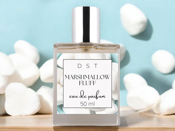 50ml bottle of Marshmallow Fluff Eau de Parfum spray sitting on a wood countertop with fluffy white marshmallows against a pale blue background.