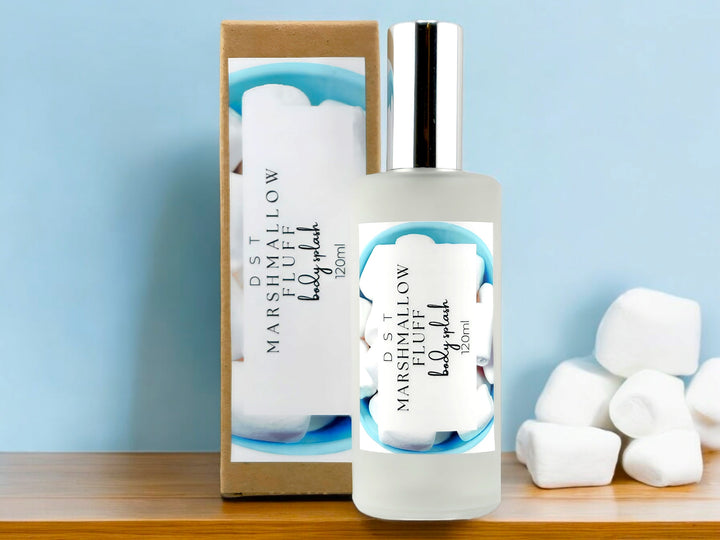 4oz bottle of Marshmallow Fluff Body Splash and the box it is packaged in sitting on wood countertop with light blue background and white marshmallows. 