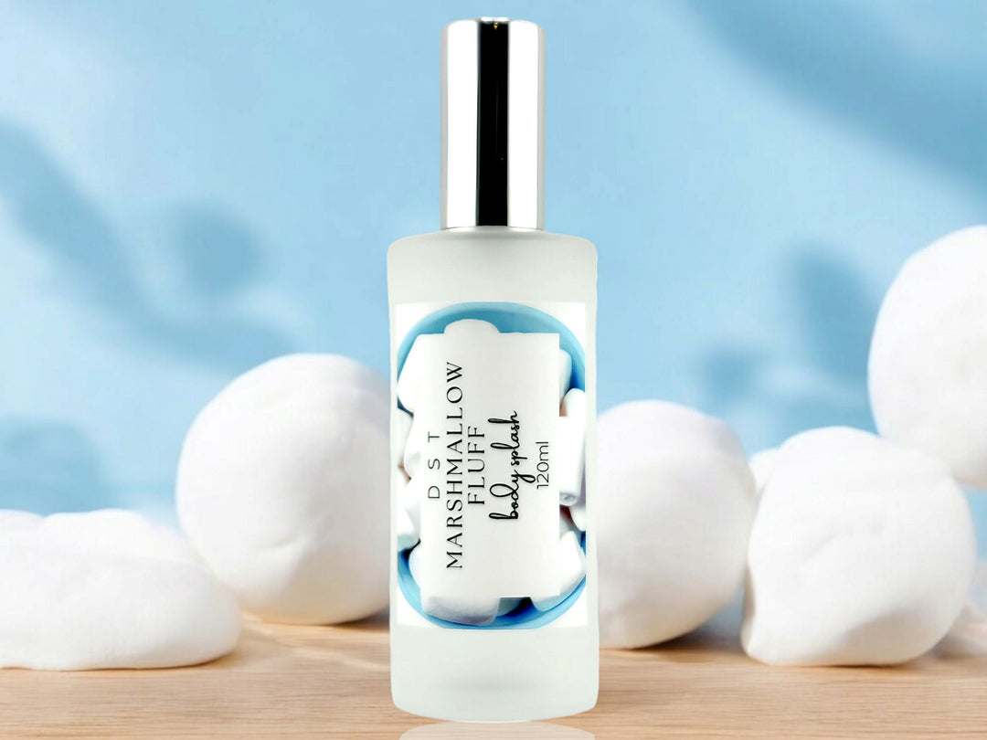 4oz bottle of Marshmallow Fluff Body Splash sitting on wood countertop with light blue background and white marshmallows. 