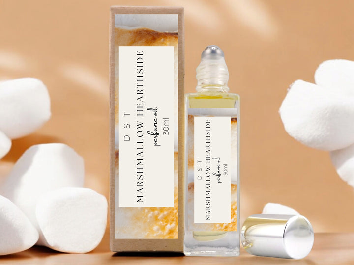 30ml bottle of Marshmallow Hearthside perfume oil and the box that it is packaged in surrounded by white puffy marshmallows against a shadowy tan background.