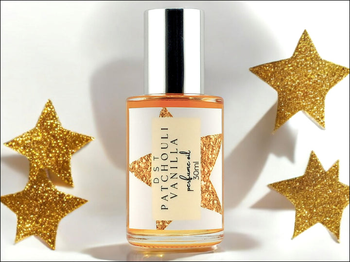 30ml bottle of Patchouli Vanilla Perfume oil sitting on white surface with gold glitter stars against a light grey shadowy background.