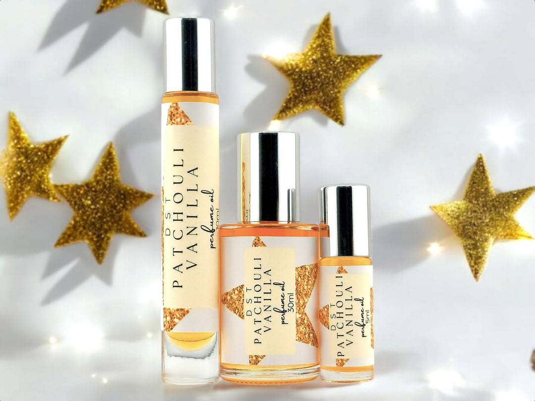 5, 10, and 30ml bottles of Patchouli Vanilla Perfume oil sitting on white surface with gold glitter stars and twinkling lights against a light grey background.