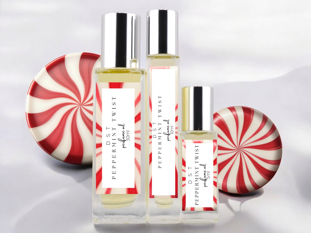 5, 10 and 30ml bottles of Peppermint Twist perfume oil sitting on wood countertop with 2 peppermint swirl candies set against white background.