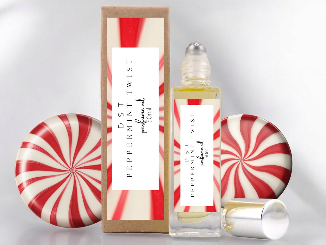 30ml bottle of Peppermint Twist perfume oil and the box it is packaged in sitting on wood countertop with 2 peppermint swirl candies set against white background.