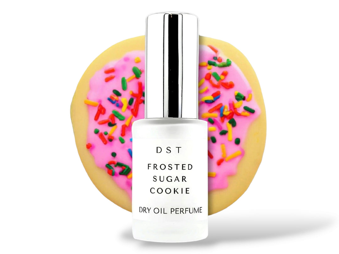 30ML bottle of Frosted Sugar Cookie Dry Oil Perfume Spray sitting in front of a large pink Frosted Sugar Cookie against a white background. 