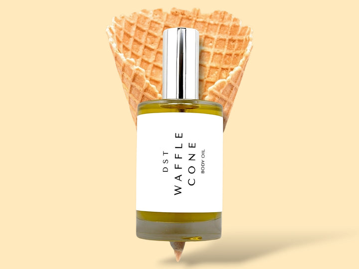 100ML bottle of Waffle Cone body oil sitting in front of a large Waffle Cone against a cream background.