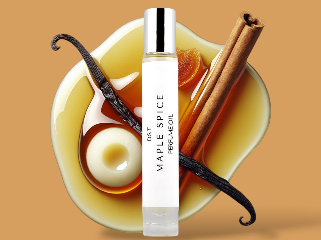 10ML bottle of Maple Spice perfume oil sitting in front of a large puddle of maple syrup, with Vanilla creme,  and vanilla bean and cinnamon stick on top against a tan background.