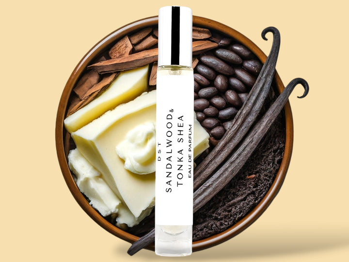 10ML bottle of Sandalwood and Tonka Shea Parfum sitting in front of a large wooded bowl filled with shea butter, tonka beans, Sandalwood, and long vanilla beans, against a tan background. 