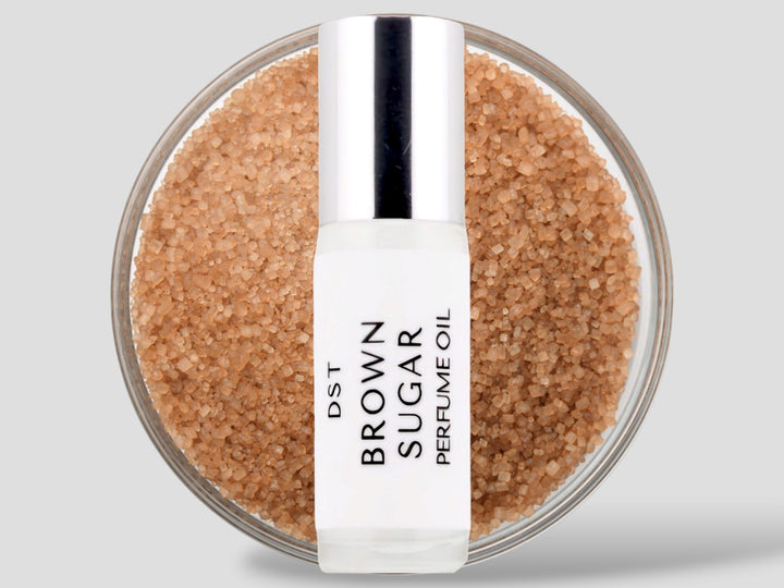 5 milliliter bottle of Brown Sugar perfume oil sitting in front of a large glass bowl filled with brown sugar against a light grey background.