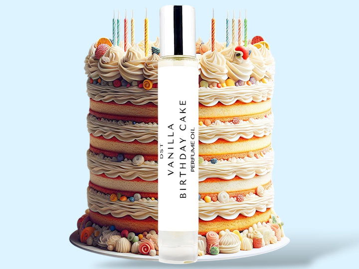 10ml bottle of Vanilla Birthday Cake Cake perfume oil sitting in front of an ornate colorful Birthday Cake topped with candles, against a light blue background.