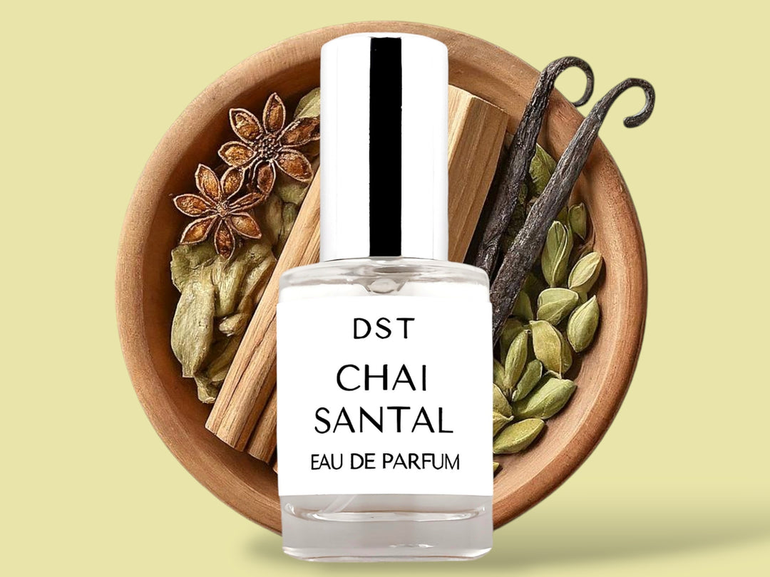 10ML bottle of Chai Santal Parfum sitting in front of a large wooded bowl filled with star anise, cardamom pods, Sandalwood, Cinnamon Sticks   and long vanilla beans, against a tan background. 