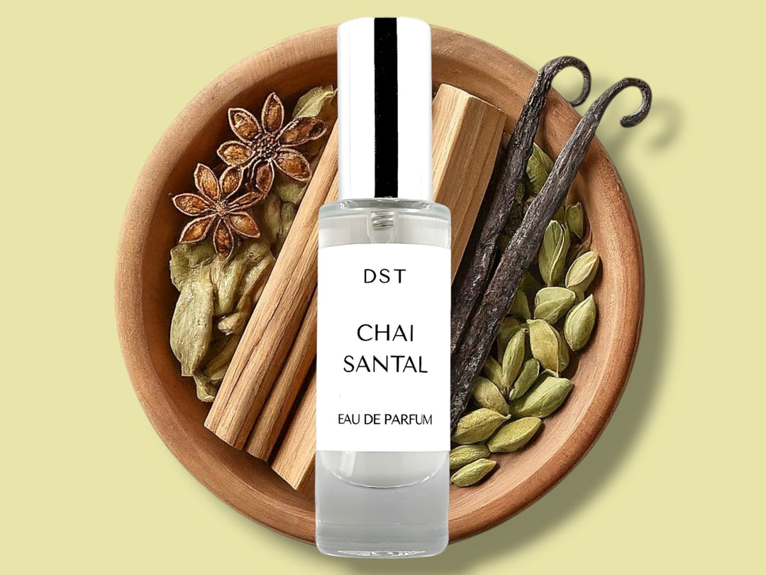 30ML bottle of Chai Santal Parfum sitting in front of a large wooded bowl filled with star anise, cardamom pods, Sandalwood, Cinnamon Sticks   and long vanilla beans, against a tan background. 