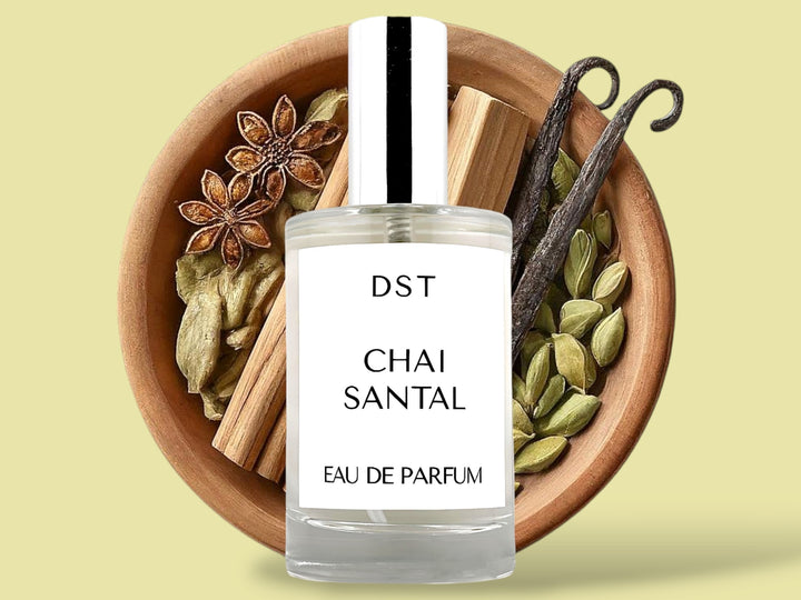 100ML bottle of Chai Santal Parfum sitting in front of a large wooded bowl filled with star anise, cardamom pods, Sandalwood, Cinnamon Sticks   and long vanilla beans, against a tan background. 