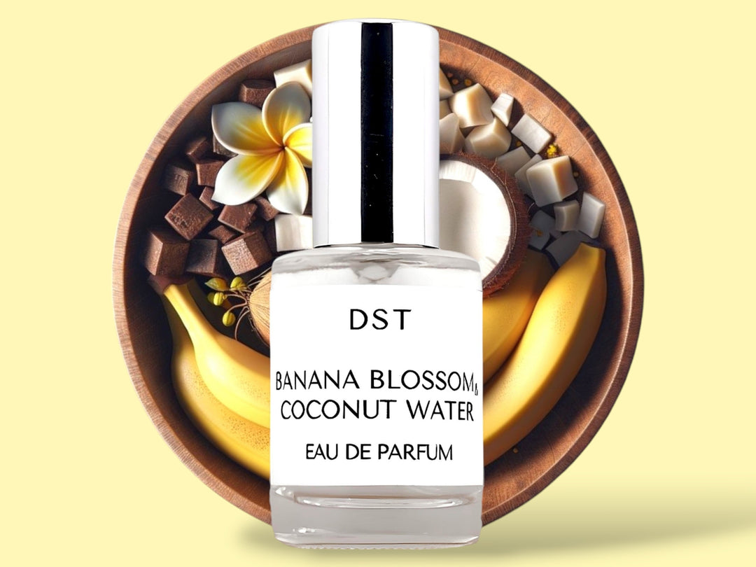 10ML bottle of Banana Blossom and Coconut Water Eau de Parfum sitting in front of a large wooden bowl filled with bananas, tiare flowers, and coconut halves, against a light yellow background. 