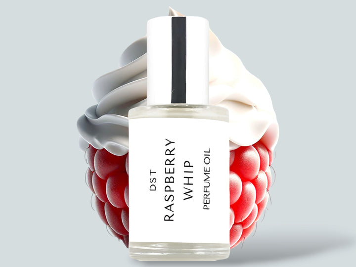 30ML bottle of Raspberry Whip perfume oil sitting in front of a large Raspberry topped with whipped cream against a light grey background. 