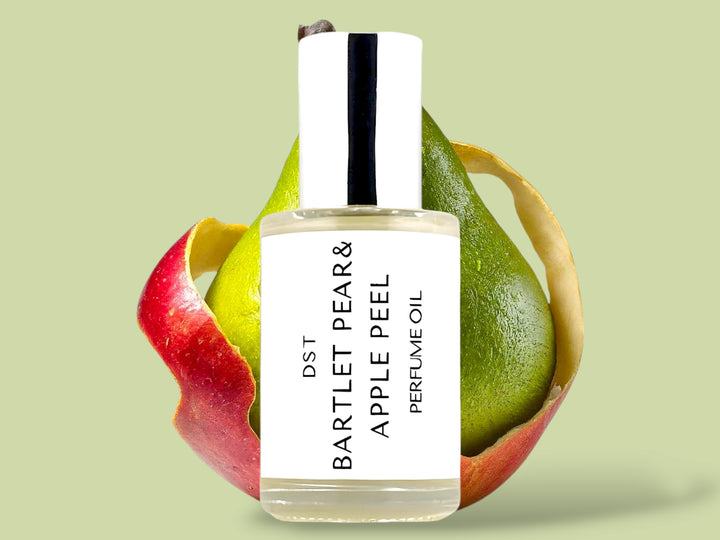 30ml bottle of Bartlet Pear and Apple Peel perfume oil sitting in front of a green pear that is wrapped in  red Apple Peel on a light green background.