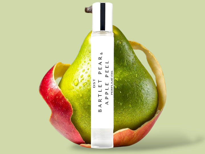 10ml bottle of Bartlet Pear and Apple Peel perfume oil sitting in front of a green pear that is wrapped in  red Apple Peel on a light green background.